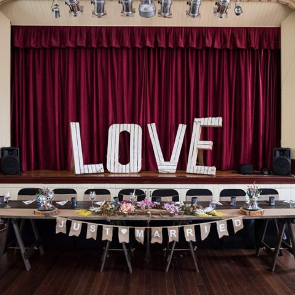Decorated stage with 'LOVE' letters and 'Just Married' banner in front of red curtains.