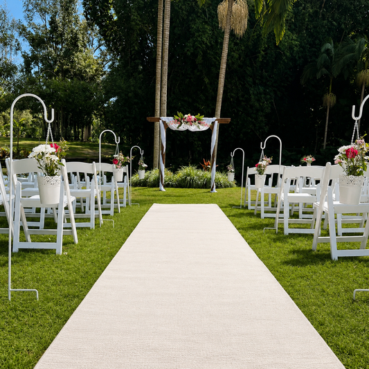 Outdoor wedding setup with white chairs, floral arrangements, and a white aisle runner.