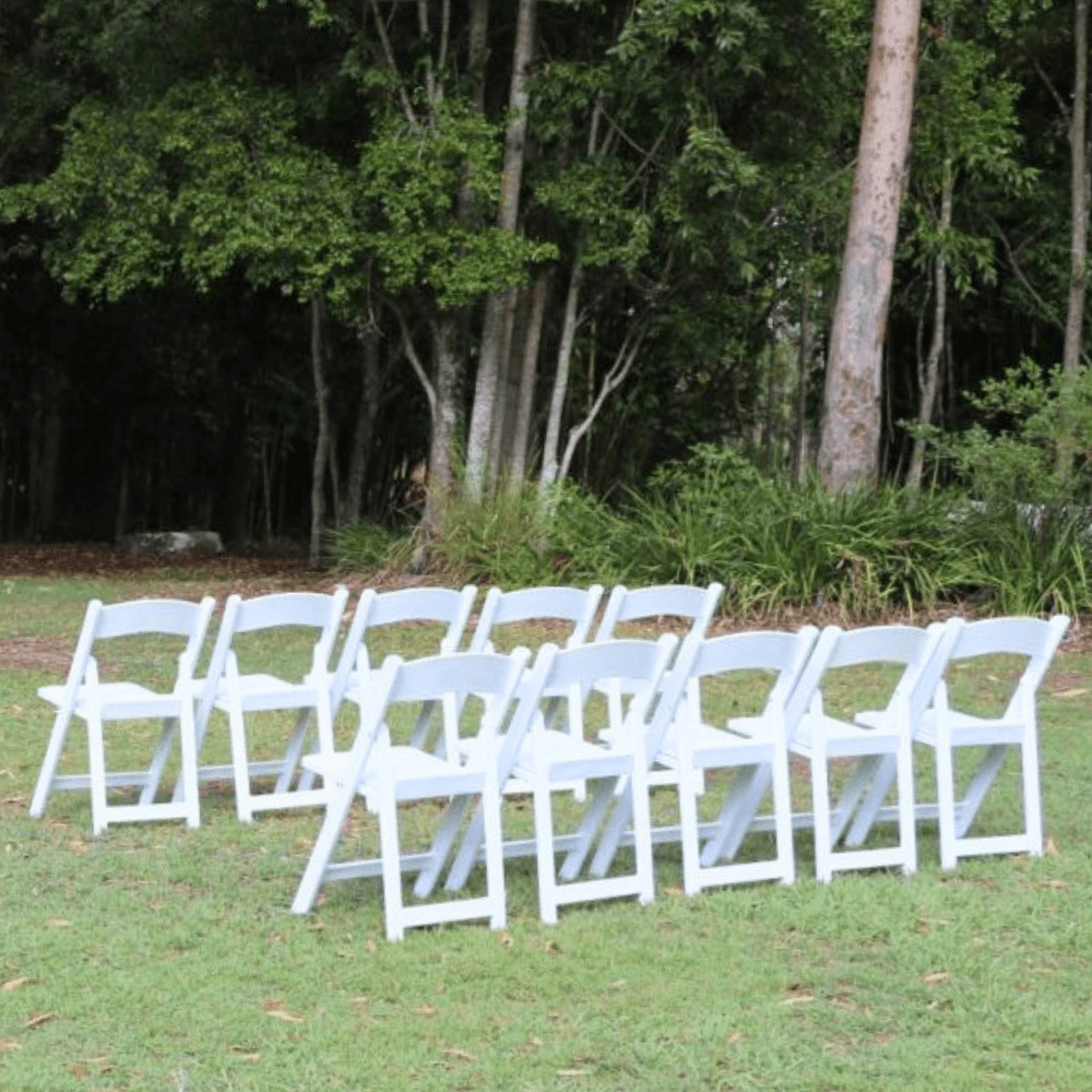 Row of white chairs set up outdoors on a grassy area with trees in the background