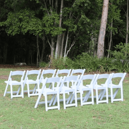 Row of white chairs set up outdoors on a grassy area with trees in the background