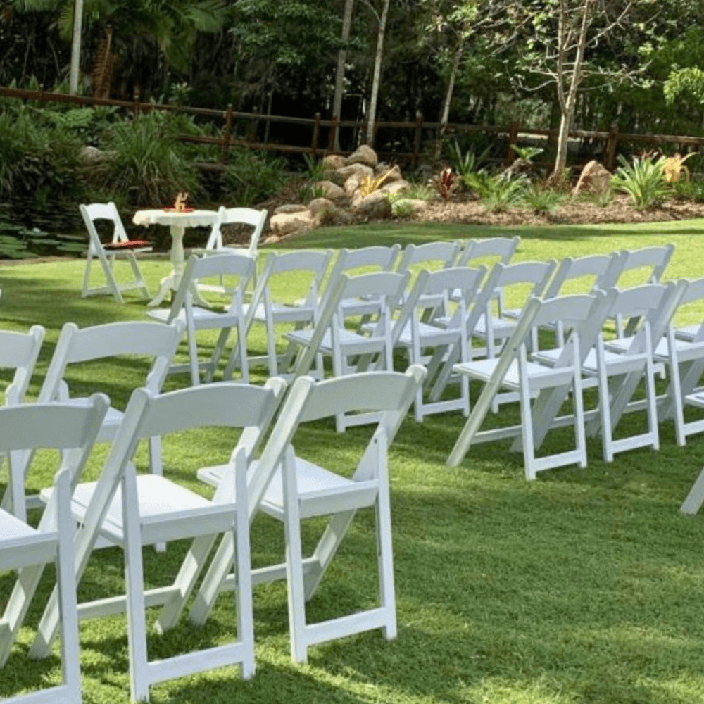 White chairs arranged in rows on a grassy area with trees in the background