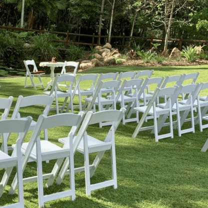 White chairs arranged in rows on a grassy area with trees in the background